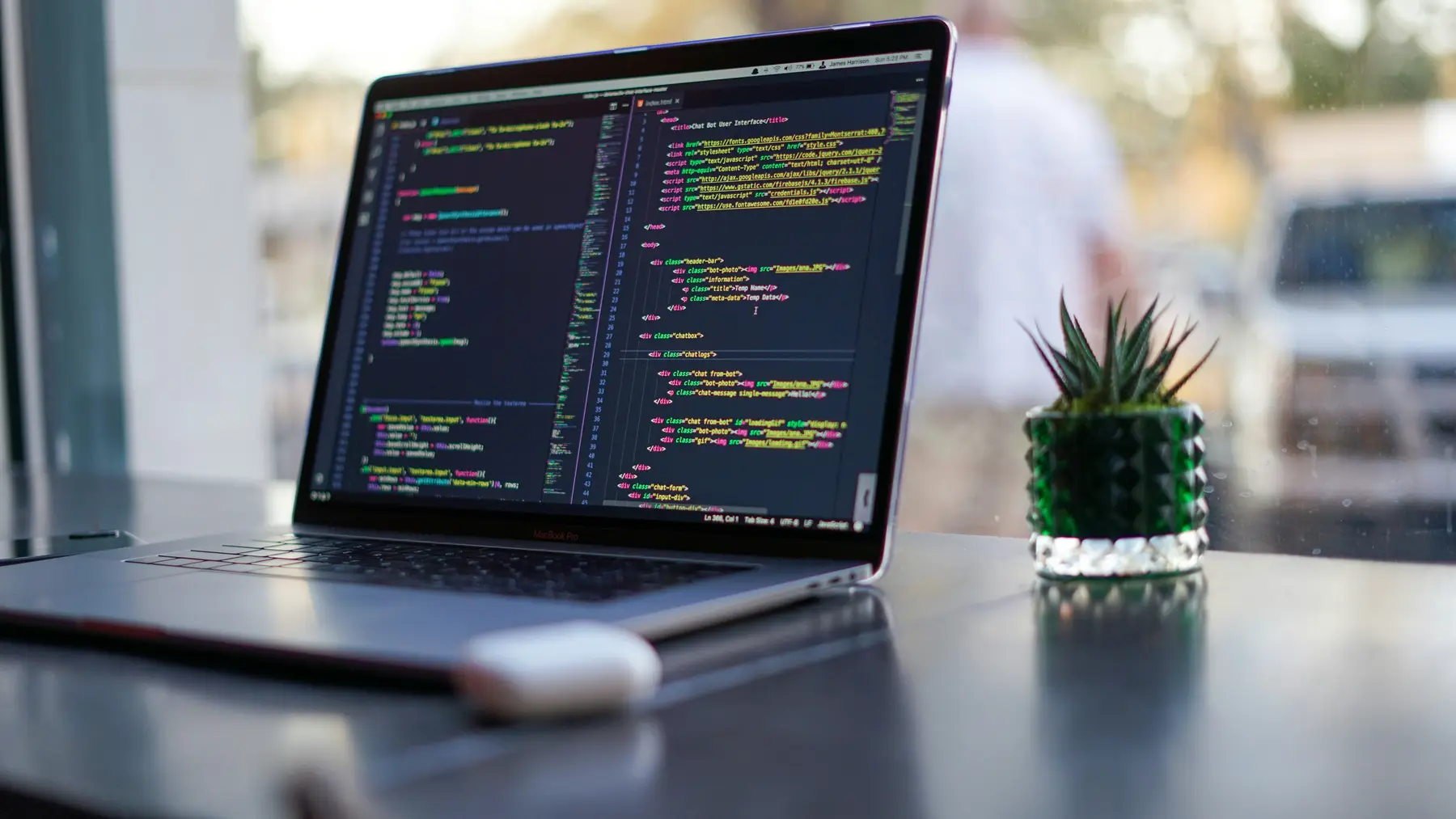 An open laptop showing code on a bright outdoor desk beside a small potted plant.