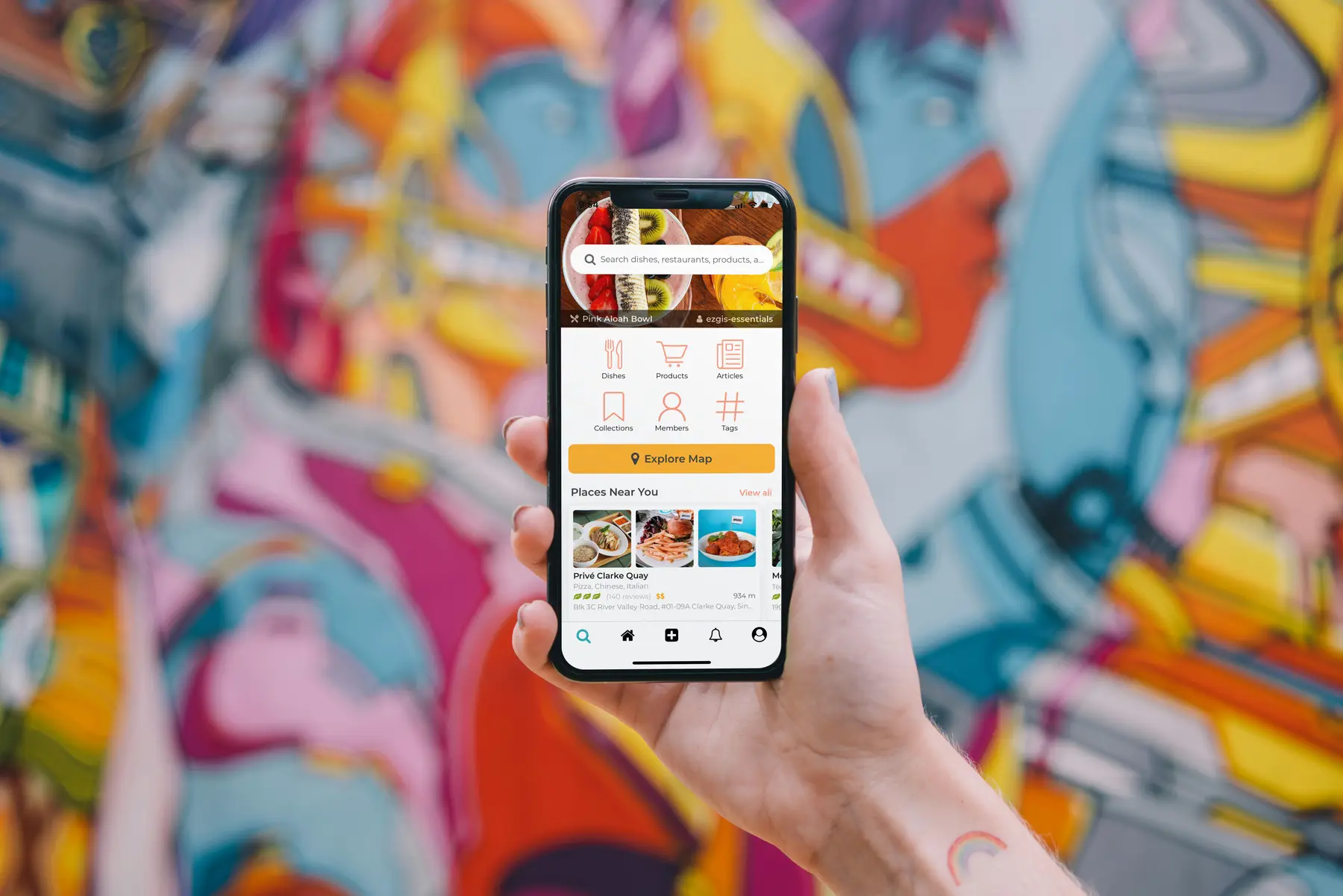 A hand holding a phone showing a mobile app, against a brightly painted mural.